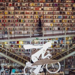 Model of a flying cyclist in front of a huge bookcase. 